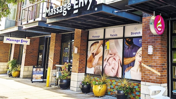 Een massagetherapiecentrum met een bord waarop 'Massage Envy' staat en een grote poster die diensten promoot.