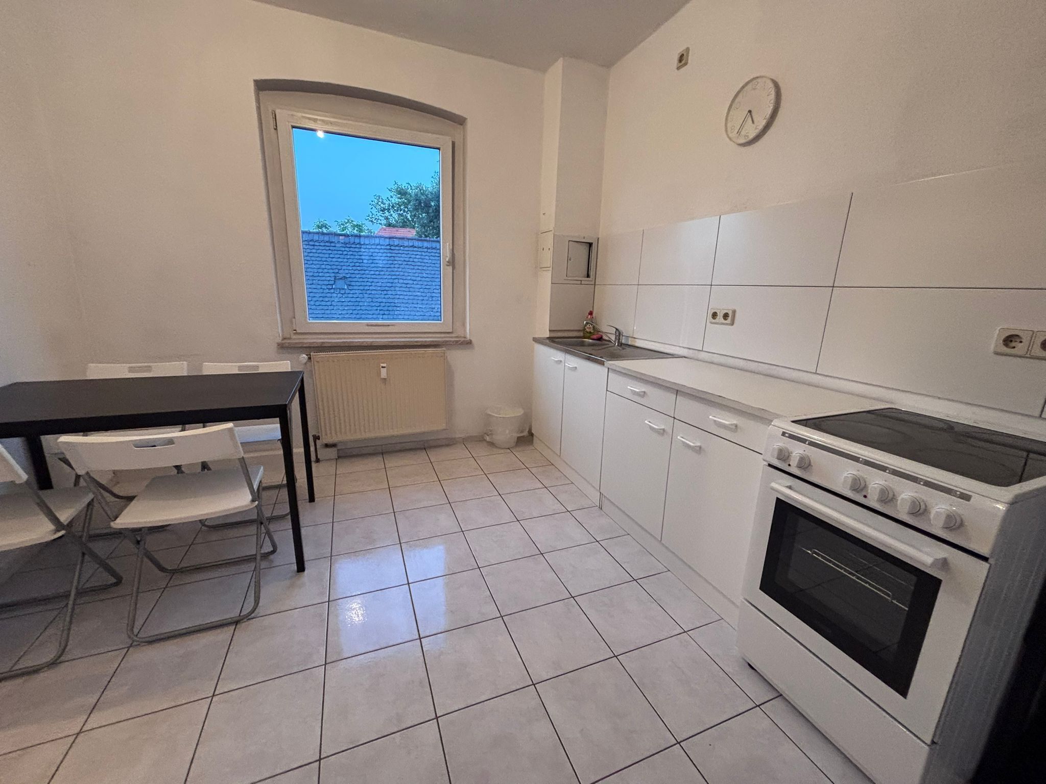 Une cuisine avec des meubles blancs, une cuisinière et une fenêtre donnant sur un mur de briques.