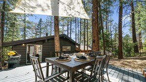Une terrasse en bois avec une table dressée pour le repas, entourée de grands arbres.