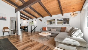 Un salon spacieux doté d’un plafond en bois, d’un canapé gris, d’une table basse ronde et d’une grande fenêtre laissant entrer la lumière naturelle.