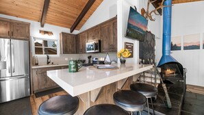 Une cuisine moderne avec des meubles en bois, des appareils en acier inoxydable, un îlot central blanc doté de tabourets de bar et une hotte de couleur bleue.