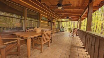 A wooden deck with a table and chairs, large windows, and a ceiling fan.
