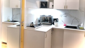 Eine kleine Küche mit weißen Schränken, einer Mikrowelle, einer Kaffeemaschine und einem Spülbecken.