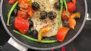 Eine Pfanne mit Fleisch, grünen Bohnen und Kirschtomaten auf einem Herd.