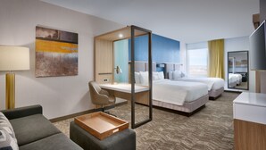 Una habitación de hotel con escritorio, dos camas, un sofá, una mesita y un ventanal grande.