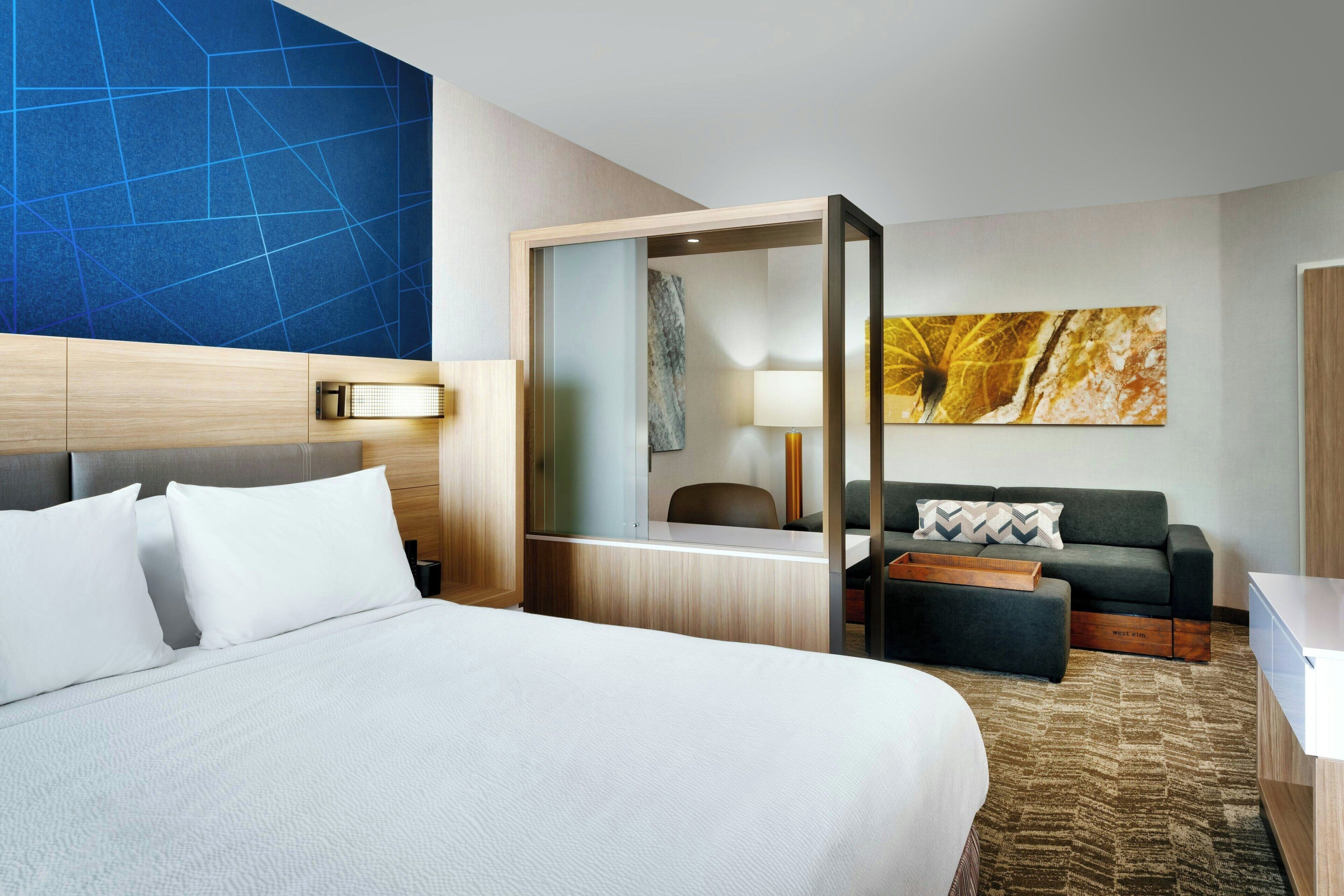 A hotel room with a large bed, a desk, a sofa, and a mirror.