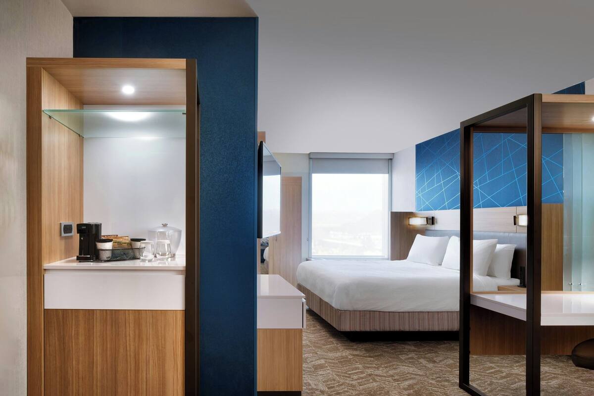 A modern hotel room with a bed, a bedside table, a mirror, and a window.