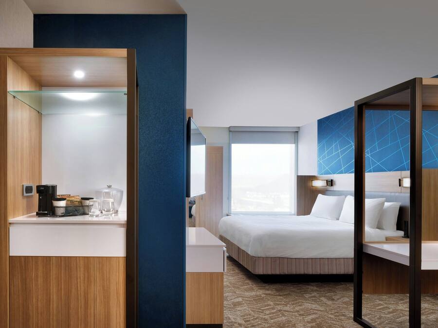 Habitación de hotel moderna con cama, mesita de noche, espejo y ventana.
