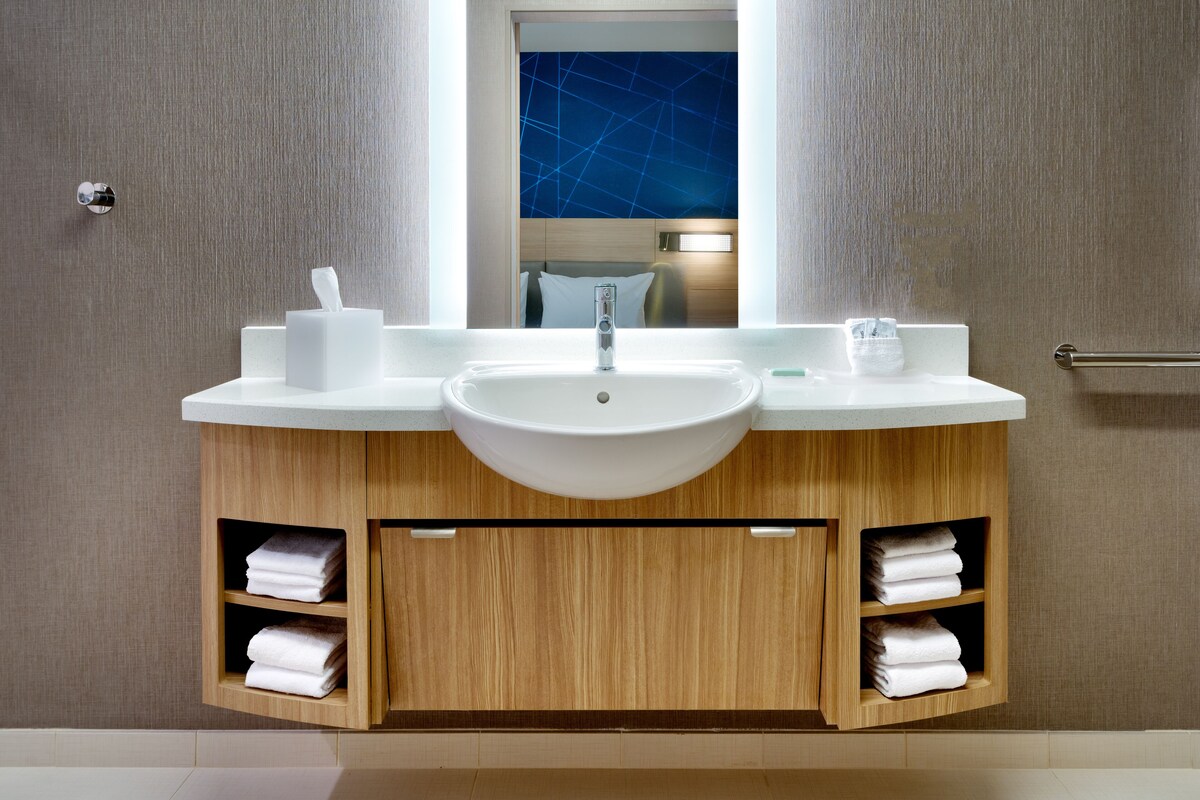 A modern bathroom with a white sink, mirror, and wooden cabinetry.