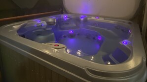 A hot tub with multiple jets, surrounded by wooden paneling and under a sloped ceiling with recessed lighting. - Lg Townhouse (Bigwhite)