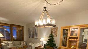 A dining area with a wooden table, chairs, and a chandelier. There is a small Christmas tree and a cabinet with glass doors. - Lg Townhouse (Bigwhite)