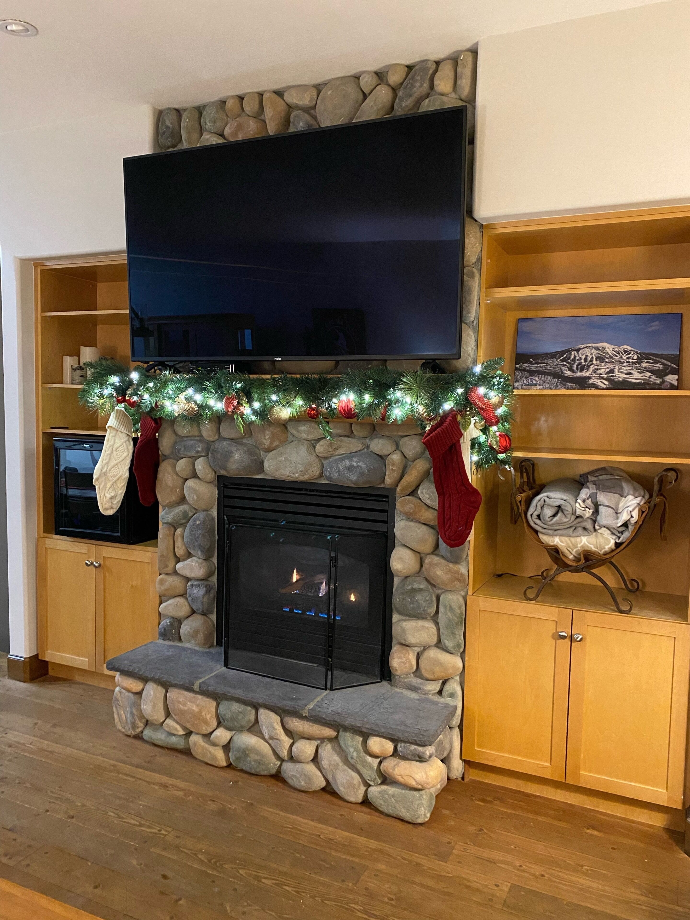 A stone fireplace with a flat-screen TV above it, surrounded by wooden cabinets and a stone shelf.
