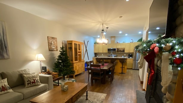 A cozy living room with a fireplace, a dining area, and a kitchen in the background. - Lg Townhouse (Bigwhite)