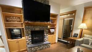 A living room with a stone fireplace, wooden shelves, a flat-screen TV, and a sofa. - Lg Townhouse (Bigwhite)