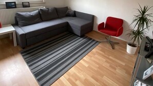 Una sala de estar moderna con un sofá seccional gris, un sillón rojo, un tapete a rayas y una planta en maceta.