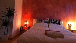 Un dormitorio con una cama grande, una mesita de noche con lámpara y una planta en maceta.