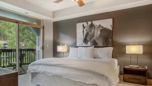 Quarto com uma cama grande, duas luminárias de cabeceira, um retrato emoldurado de um cavalo e vista para uma varanda com mobiliário.