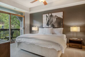 Relax in this serene bedroom with a large bed, bedside tables, and a framed picture above, leading to an outdoor space with a deck and chairs.