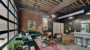 A modern living room with a green sofa, leather armchairs, a coffee table, and a large window. - One-Of-A-Kind! Roll Up Garage Door, Pool, Speakeasy (Nashville)