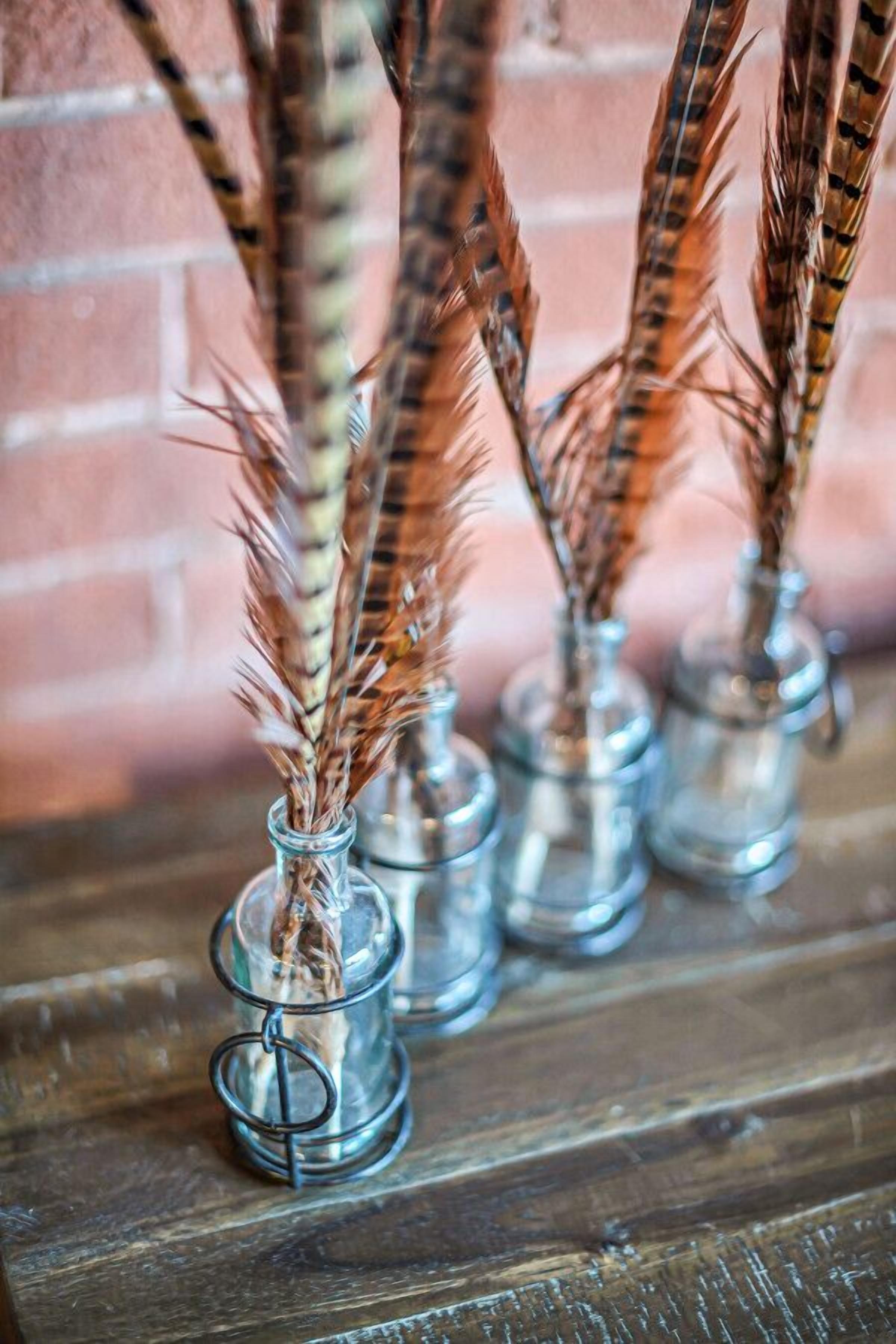 Four glass vases with dried wheat stalks on a wooden surface.