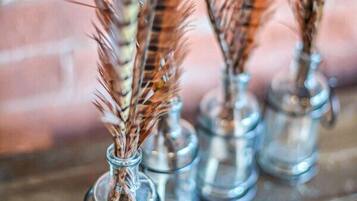 Four glass vases with dried wheat stalks on a wooden surface.