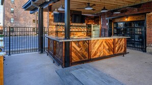 An outdoor bar area with a wooden counter and hanging lights, adjacent to a brick building. - One-Of-A-Kind! Roll Up Garage Door, Pool, Speakeasy (Nashville)