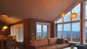 A cozy living room with a brown leather sofa, a wooden coffee table, and a view of mountains through large windows. - Beautiful Mountaincabin at Lifjell (Vestfold og Telemark)