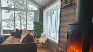 A cozy room with a sofa, a chair, a fireplace, and large windows overlooking a snowy landscape. - Beautiful Mountaincabin at Lifjell (Vestfold og Telemark)