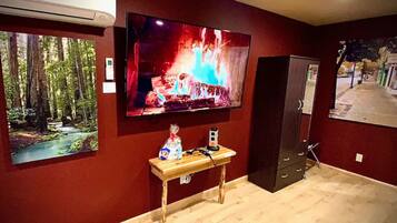 Ein Zimmer mit an der Wand befestigtem Fernseher, der eine Feuerszene zeigt, einem kleinen Tisch mit einer Tasche und einem Gerät sowie einem Waldposter.