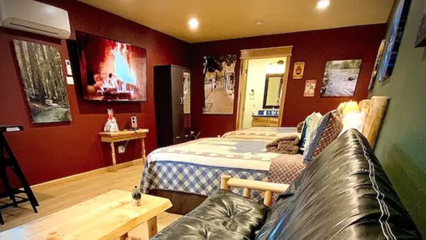 A cozy room with a bed, a wooden table, and a leather couch. - Cedar Mountain - Suite E (Grants Pass)