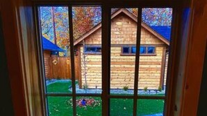 A window with a view of a wooden cabin and a green lawn. - Cedar Mountain - Suite E (Grants Pass)