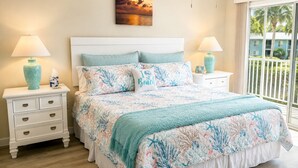 Une chambre à coucher avec un lit, deux tables de chevet, un ventilateur de plafond, une fenêtre donnant sur un beau paysage et un tableau accroché au mur.