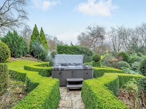 A hot tub in a garden with hedges and trees.