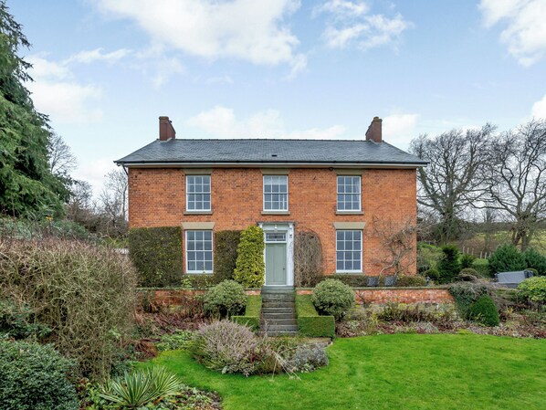 A two-story brick house with a front door, a small front garden, and a paved driveway.