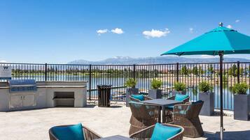 Un patio al aire libre con una parrilla, asientos y vistas a un lago y montañas.