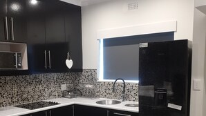 A modern kitchen with dark cabinets, a black refrigerator, a microwave, and a granite countertop backsplash. - Marina Glen Resort No.46 (Southbroom)
