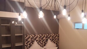 A bedroom with a herringbone-patterned headboard, a bed with white linens, and multiple hanging light bulbs. - Marina Glen Resort No.46 (Southbroom)