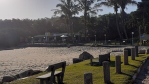 A beachside area with a wooden bench, a pathway, and a building with outdoor seating. - Marina Glen Resort No.46 (Southbroom)