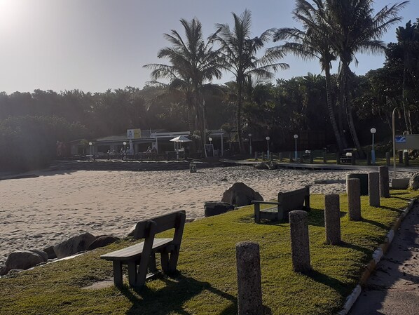 A beachside area with a wooden bench, a pathway, and a building with outdoor seating.