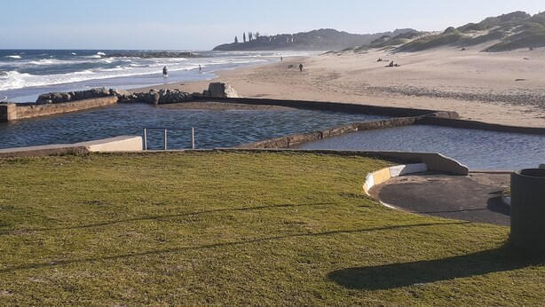 A beach with rocky breakwaters, a grassy area, and a sandy shore. - Marina Glen Resort No.46 (Southbroom)