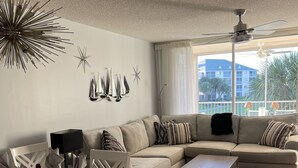 Uma sala de estar com sofá, mesa de jantar posta para refeição e vista para o exterior.