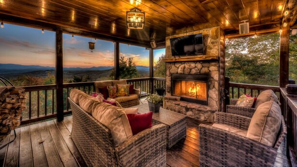 A cozy outdoor seating area with wicker furniture, a stone fireplace, and a view of the mountains.