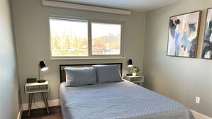 Une chambre à coucher avec un lit, deux tables de chevet, une fenêtre et deux tableaux abstraits accrochés au mur.