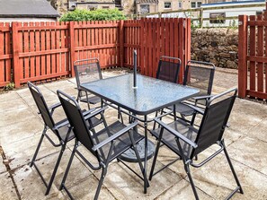 A glass-top table with four chairs, a red wooden fence, and a stone wall in the background. - A spacious house in an ideal location, across the road from the beach. (Kirkcaldy)