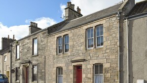 A stone building with multiple windows and doors, a red door, and a vehicle parked on the street. - A spacious house in an ideal location, across the road from the beach. (Kirkcaldy)