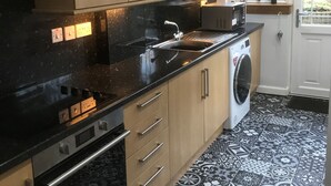 A kitchen with a washing machine, a sink, and a window with a view of a garden. - A spacious house in an ideal location, across the road from the beach. (Kirkcaldy)