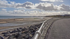 A coastal road with a guardrail, rocky beach, and the sea in the background. - A spacious house in an ideal location, across the road from the beach. (Kirkcaldy)