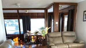 A spacious living room with a large beige sectional sofa, a smaller sofa, and a wooden coffee table. The room has wooden flooring and a view of the outdoors through a large window. - Entire House, close to downtown, airport, masters and Fort Eisenhower. (Augusta)
