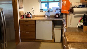 A compact kitchen with a refrigerator, dishwasher, and stove. A window with a view of the outside is visible, and an orange apron hangs on the door. - Entire House, close to downtown, airport, masters and Fort Eisenhower. (Augusta)