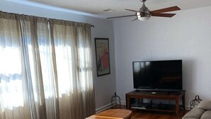 A living room with a wooden floor, a ceiling fan, a flat-screen TV, a coffee table, and two sofas. - Entire House, close to downtown, airport, masters and Fort Eisenhower. (Augusta)